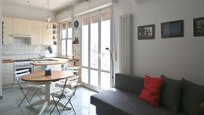 Eine moderne Küche mit Essbereich, ein graues Sofa mit einem roten Kissen und ein großes Fenster mit Blick.