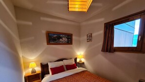 A bedroom with a bed, two bedside lamps, a window with curtains, a framed picture on the wall, and a wooden nightstand. - Apartment close to slopes - 4 guests (Arêches-Beaufort)
