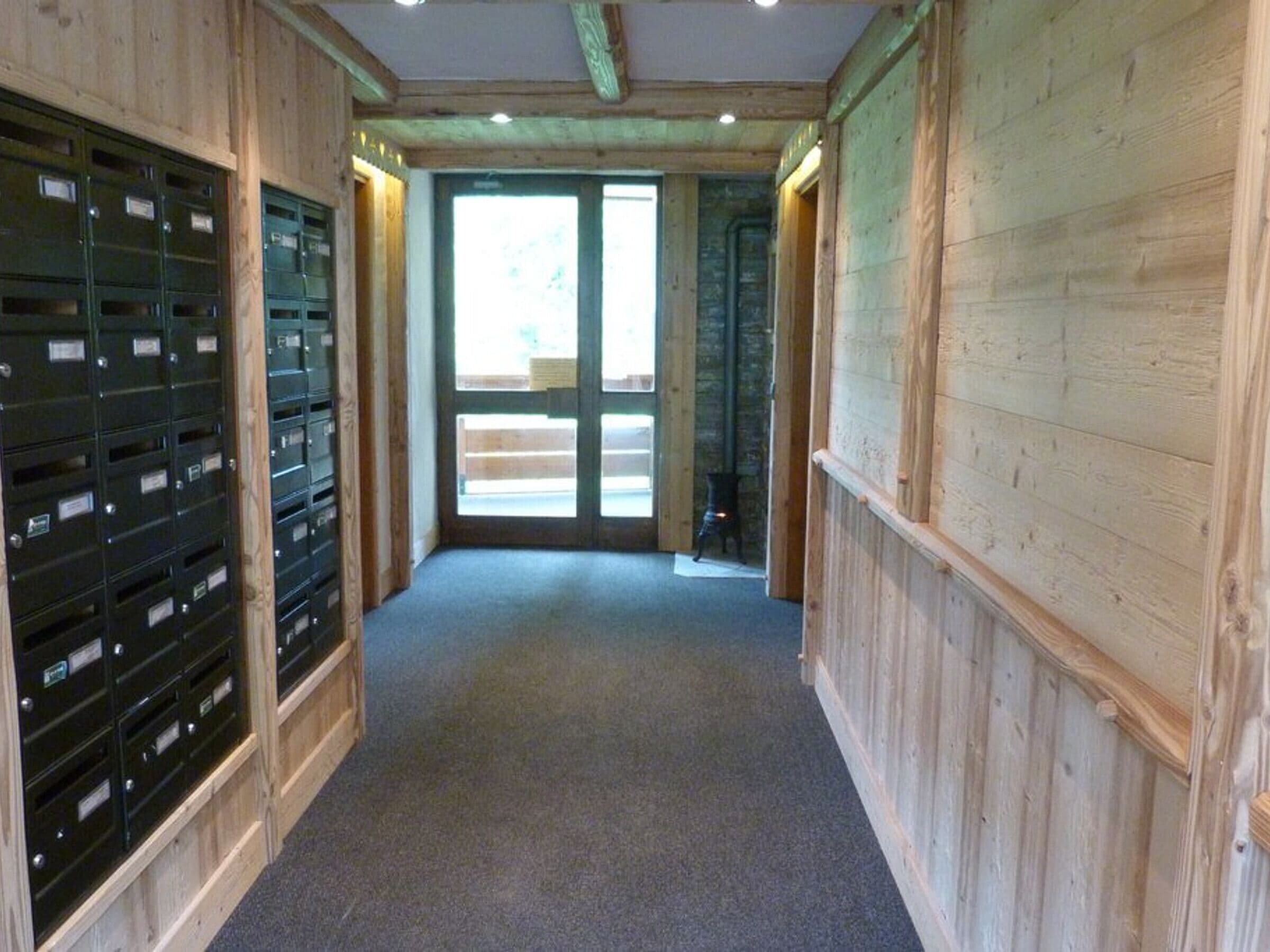 Un couloir aux murs en bois, doté d’un sol recouvert de moquette et d’une rangée de boîtes aux lettres sur le côté gauche.