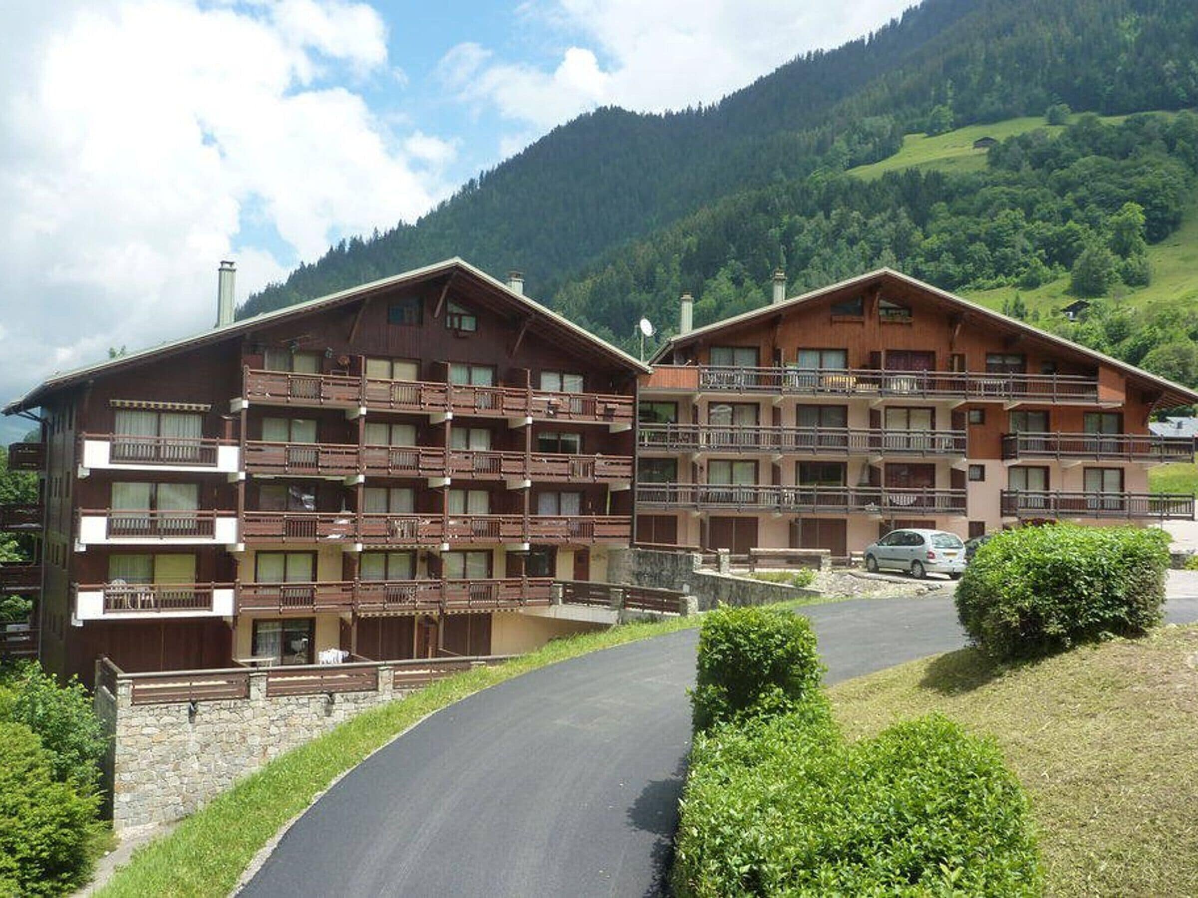 A multi-story hotel with balconies, set against a mountainous backdrop.