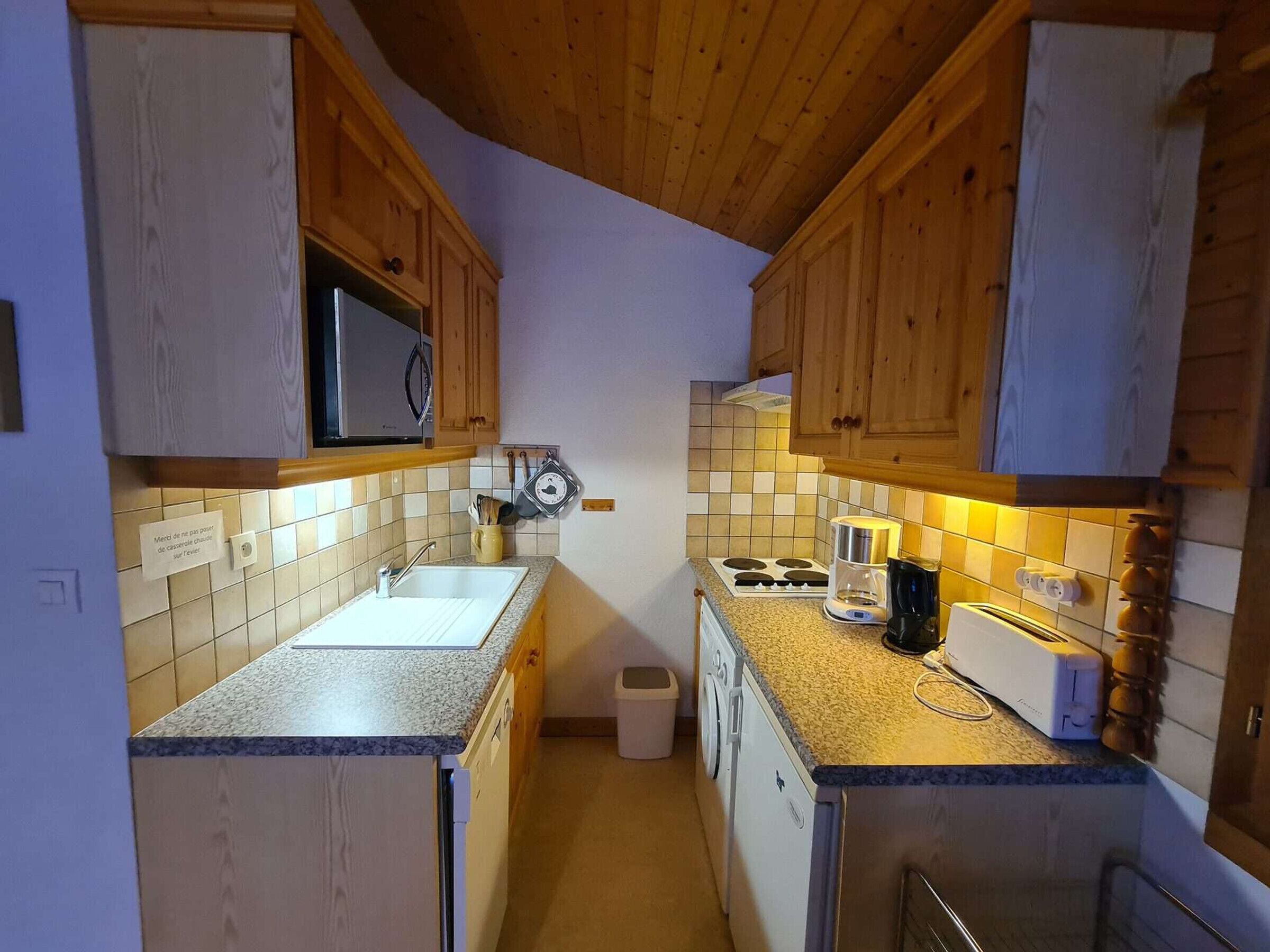A compact kitchen with wooden cabinets, a microwave, a sink, a stove, and a coffee maker.