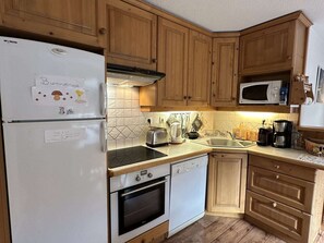 A kitchen with wooden cabinets, a white refrigerator, a microwave, a toaster, a kettle, and a sink. - Apartment with stunning village view - 7 guests (Arêches-Beaufort)