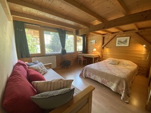Ein gemütliches Blockhauszimmer mit einem Bett, einer Couch, einem Schreibtisch und einem Sessel.