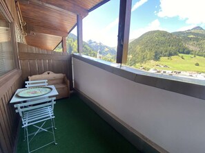 Ein Balkon mit einer Holzbank und einem Tisch mit Blick auf eine gebirgige Landschaft.