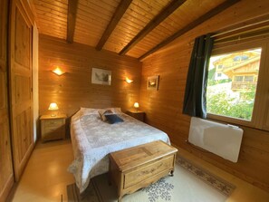 Ein Zimmer in einer Holzhütte mit einem Bett, Nachttischen, einem Fenster mit Blick und einer Heizung.