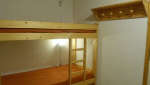 Uma cama beliche com escada, uma prateleira de madeira acima e uma tomada na parede.