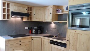 Eine kleine Küche mit Holzausstattung, einem Backofen, einer Spülmaschine und einer Kaffeemaschine.