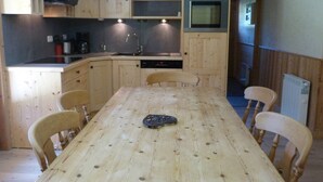 Eine kompakte Küche mit Holzschränken, einem eingebauten Backofen, einem Spülbecken und einem Esstisch mit vier Stühlen.
