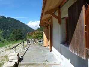 Una escalera de piedra que conduce a un edificio de madera con un muro de piedra y vista a una montaña boscosa.
