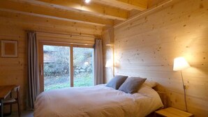 Ett sovrum i en stuga med träpanel, en säng, två sänglampor och utsikt genom ett stort fönster.