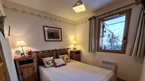 Ein Schlafzimmer mit einem Bett, zwei Nachttischen mit Lampen, einem gerahmten Bild an der Wand, einem Fenster mit Vorhängen und einem Heizkörper.