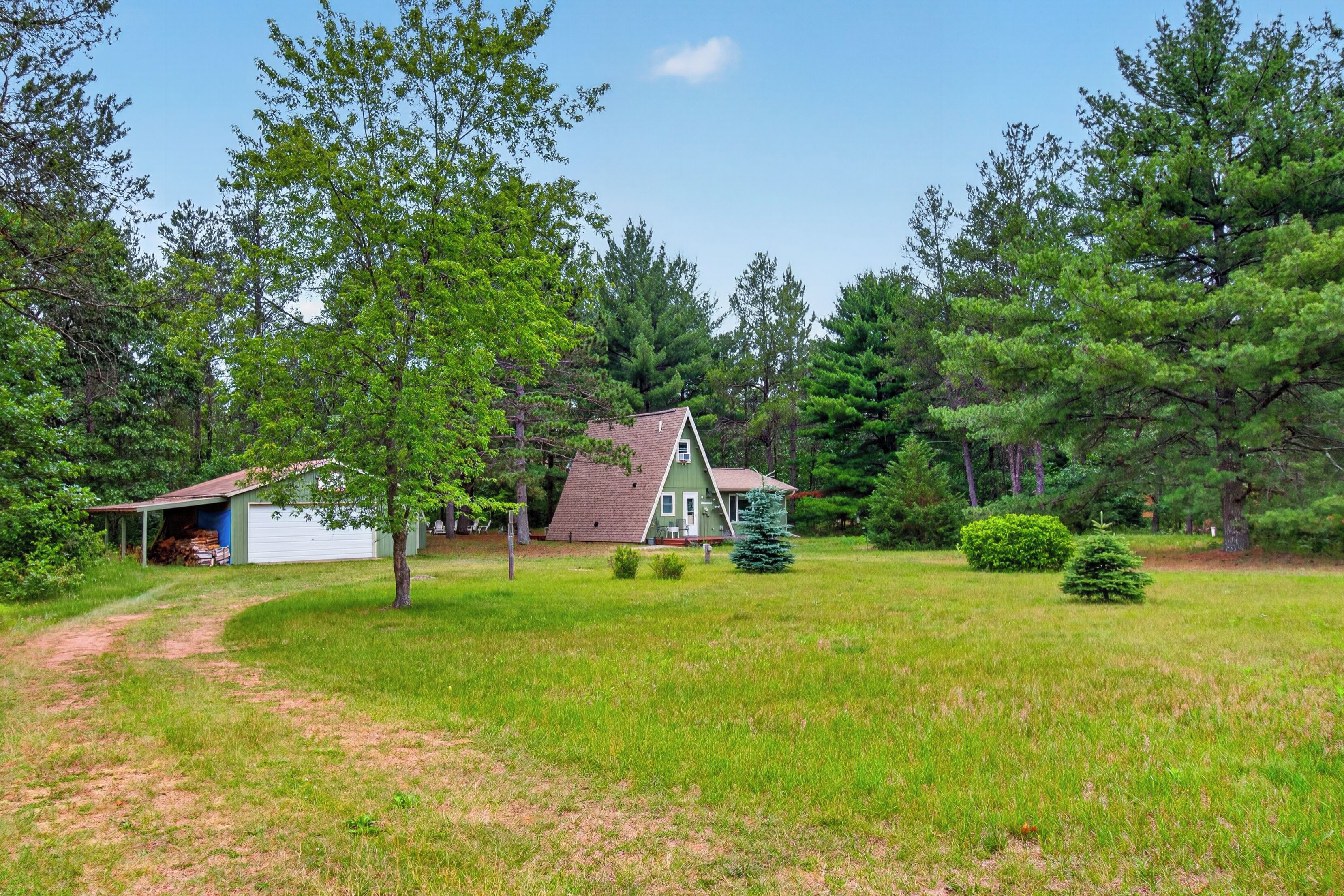 A house with a sloped roof, surrounded by a grassy yard and dense trees.
