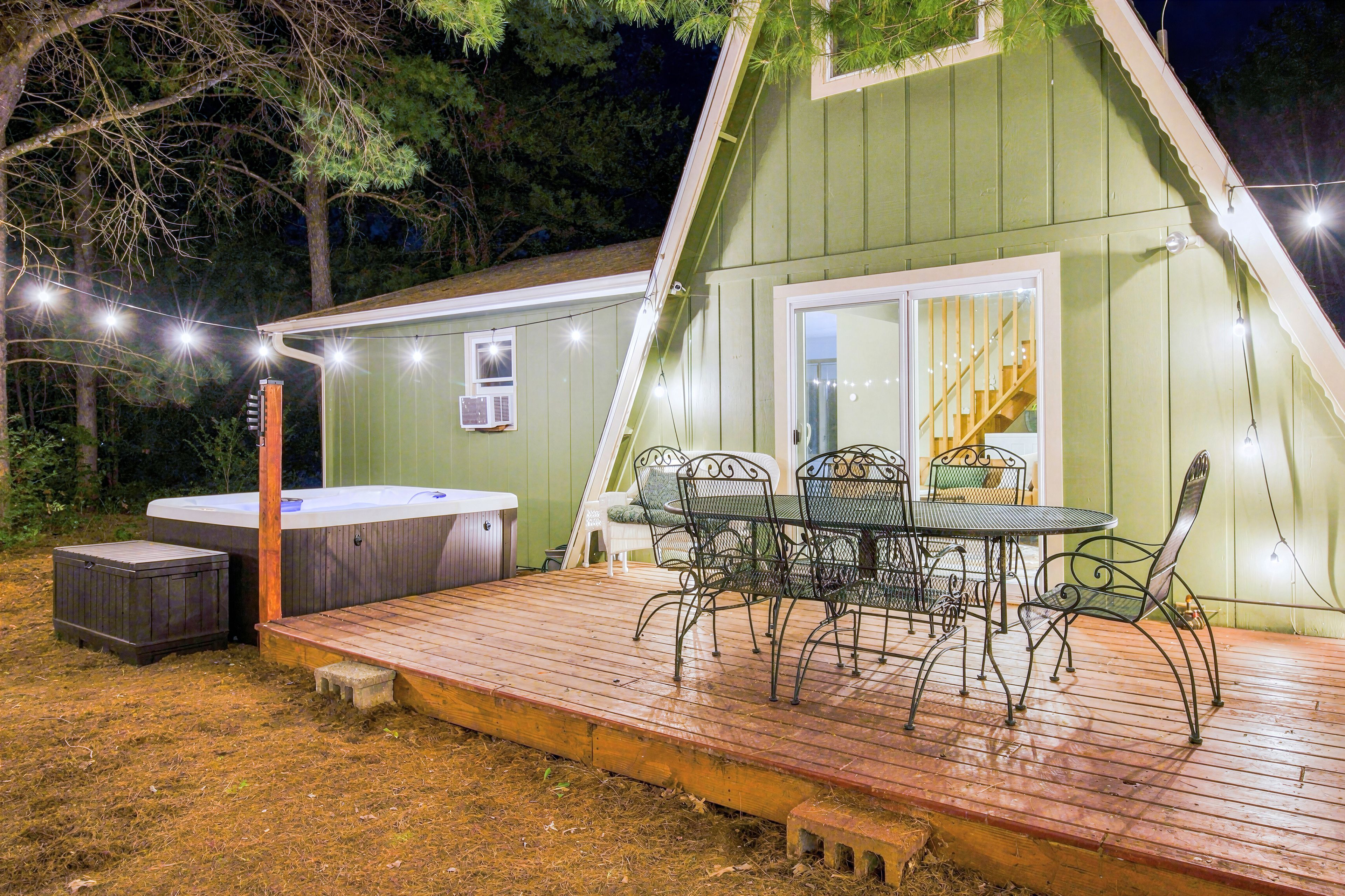Una terraza exterior acogedora con un jacuzzi, una mesa con sillas y luces colgantes.