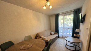 A cozy room with a wooden table, a sofa, and a TV mounted on the wall. - Cozy apartment in village center - 4 guests (Arêches-Beaufort)