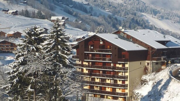A multi-story hotel with balconies, set against a snowy mountain backdrop. - Cozy apartment in village center - 4 guests (Arêches-Beaufort)