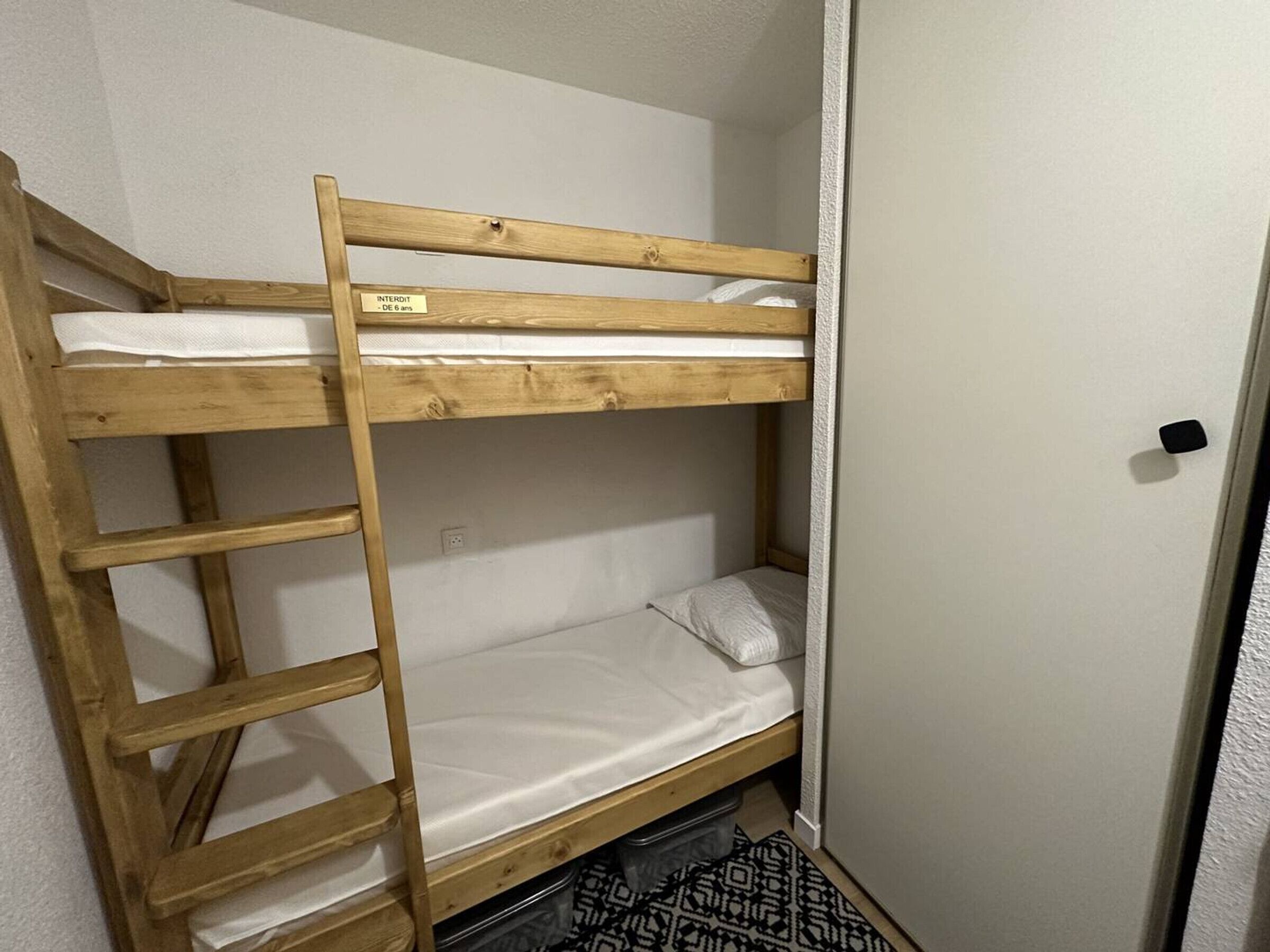 A bunk bed with a ladder, a white wall, and a door.