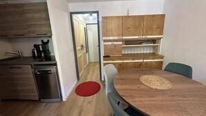 A compact kitchen with modern appliances, a dining area with a round table, and a hallway leading to a bedroom. - Cozy apartment in village center - 4 guests (Arêches-Beaufort)
