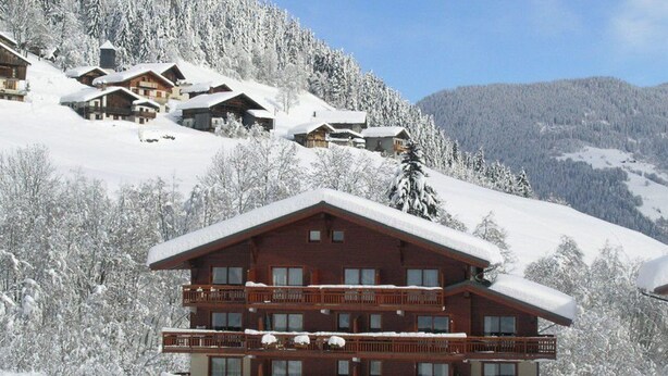 Una cabaña de varios pisos con balcones, rodeada de árboles nevados y montañas.