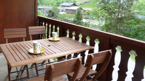 A wooden table and chairs on a balcony with a view of a green landscape and buildings. - Charming central apartment - 4 guests (Arêches-Beaufort)