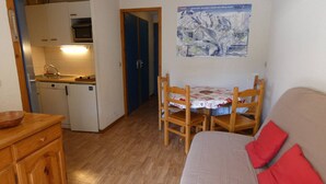 A compact living space with a kitchenette, a dining area with a table and chairs, and a sofa with red cushions. - Charming central apartment - 4 guests (Arêches-Beaufort)