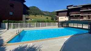 A swimming pool with a white fence, a building with balconies, and a mountainous landscape in the background. - Charming central apartment - 4 guests (Arêches-Beaufort)