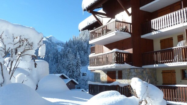 Un edificio de madera de varios pisos con balcones, rodeado de árboles y montañas cubiertas de nieve.