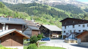 Un pueblo de montaña con edificios de madera tradicionales, una calle principal y un paisaje montañoso de fondo.