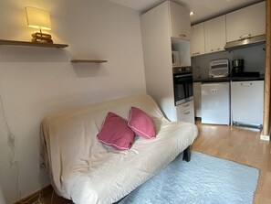 A bedroom with a bed, a bedside lamp, a kitchen area with appliances, and a small shelf. - Apartment pets welcome - 6 guests village center (Arêches-Beaufort)