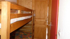 Una cama litera con cabecera de madera, una puerta con manija y un tapete de colores con motivos.