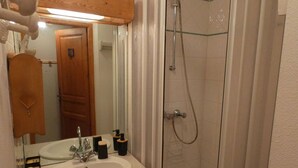 A bathroom with a white sink, a mirror, a shower with a glass door, and wooden cabinets. - Cosy apartment with beautiful view - 4 guests (Arêches-Beaufort)