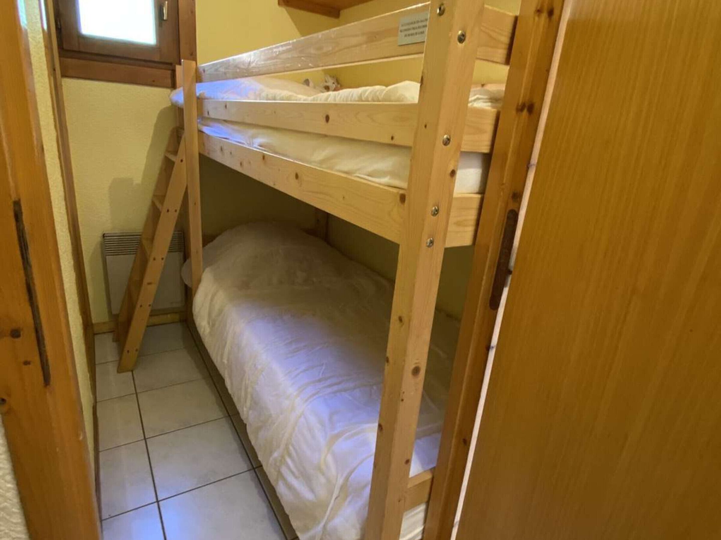Un letto a castello con una finestra sopra il letto superiore, un pavimento piastrellato e un telaio di legno.