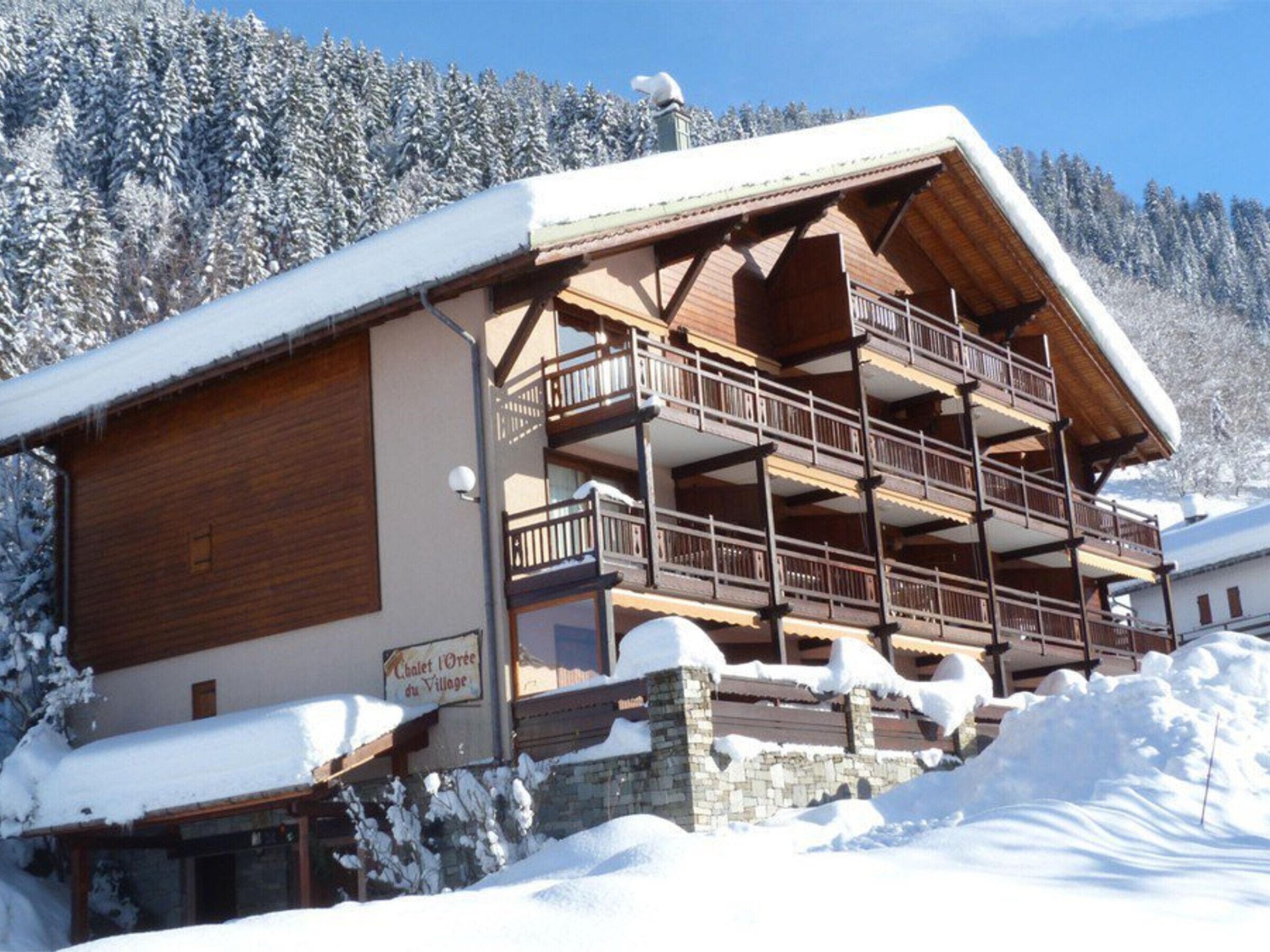 A chalet-style building with a wooden facade, stone foundation, and a balcony with railings.