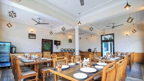 Un espace repas avec des tables et des chaises en bois, des ventilateurs de plafond et des luminaires suspendus.