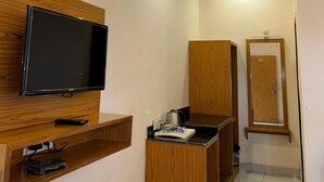 Une chambre moderne dotée d’un téléviseur à écran plat fixé sur un panneau en bois, d’une machine à café posée sur le comptoir, d’une armoire en bois et d’une porte avec un panneau en bois.