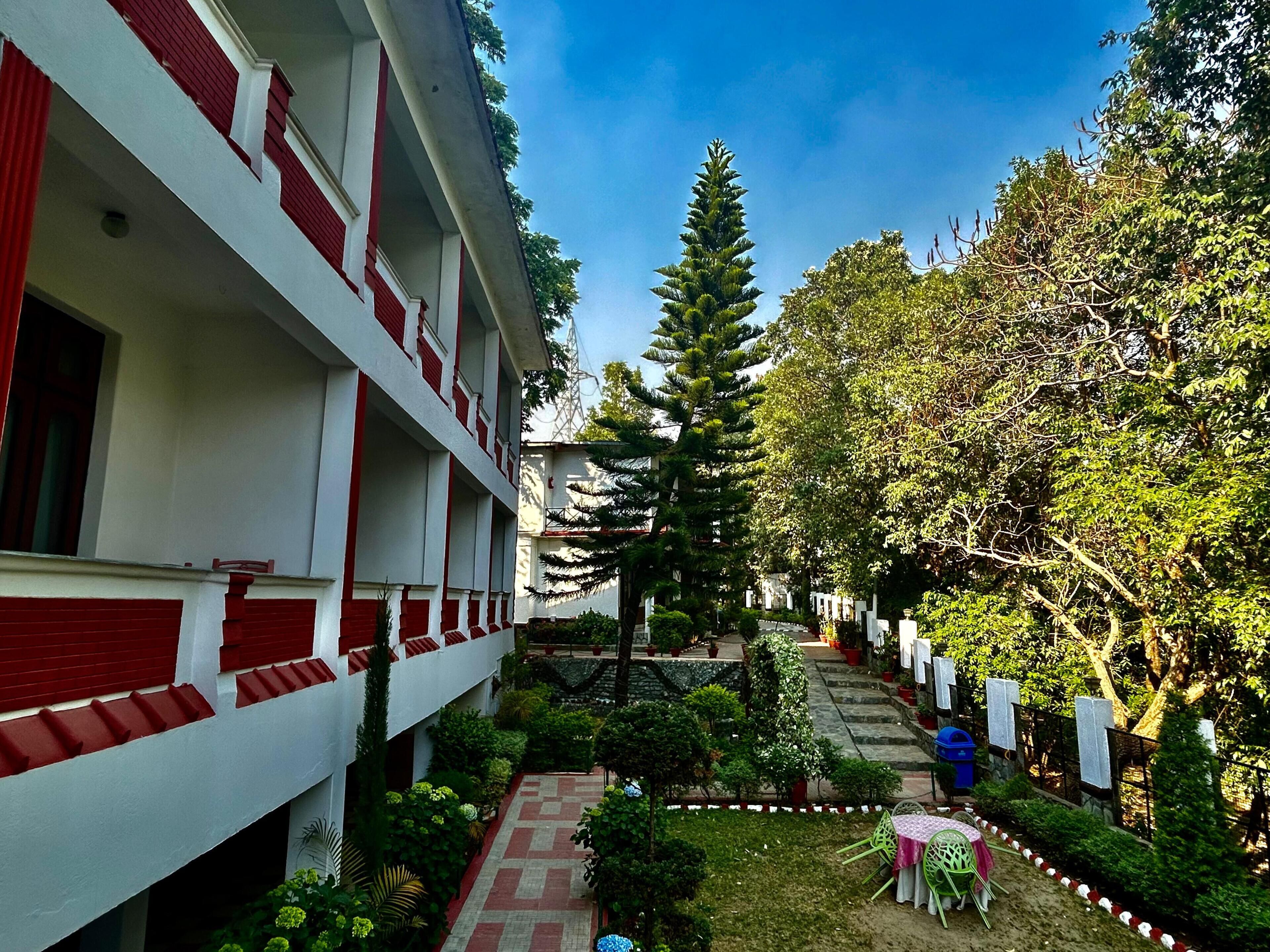 Um pátio com um edifício de paredes externas em vermelho e branco, um caminho central e vegetação ao redor.