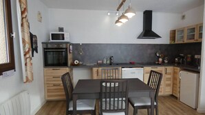 Moderni keittiö, jossa on ruokapöytä, tuolit, mikroaaltouuni, uuni ja musta liesituuletin.