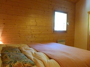 A wooden cabin room with a bed, a window, and a heater. - Spacious chalet, pets welcome - 8 guests (Arêches-Beaufort)