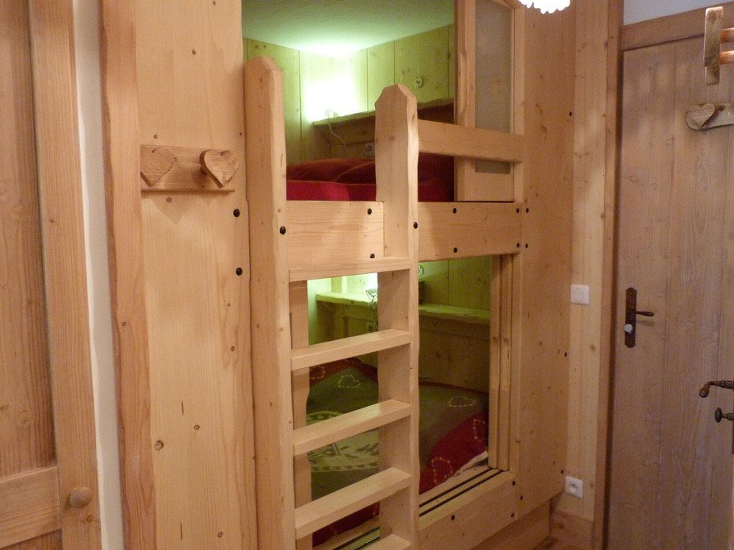 A wooden bunk bed with a ladder, a small shelf, and a door with a handle.
