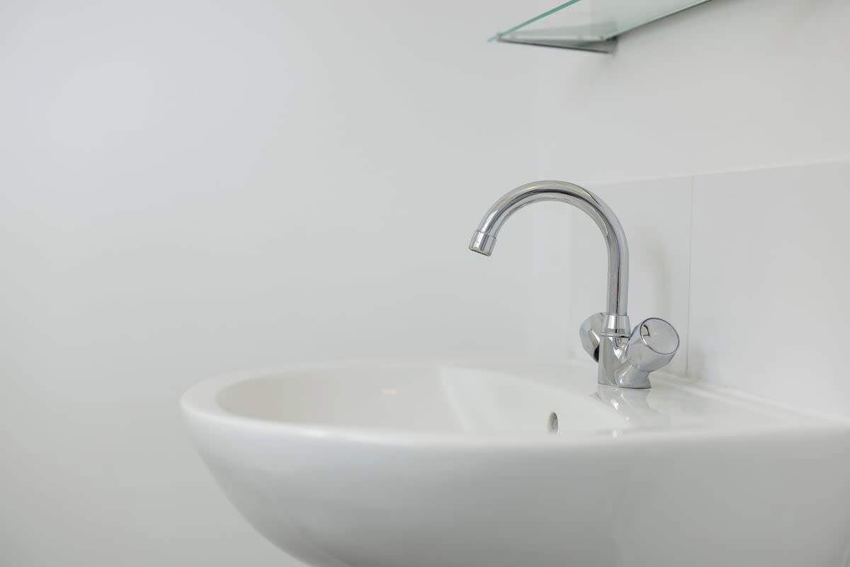 Ein weißes Waschbecken mit Chromarmatur und einer Glasablage darüber.