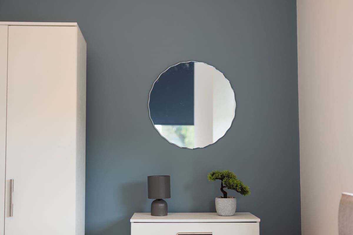 A room with a white cabinet, a round mirror, a lamp, and a small potted plant.