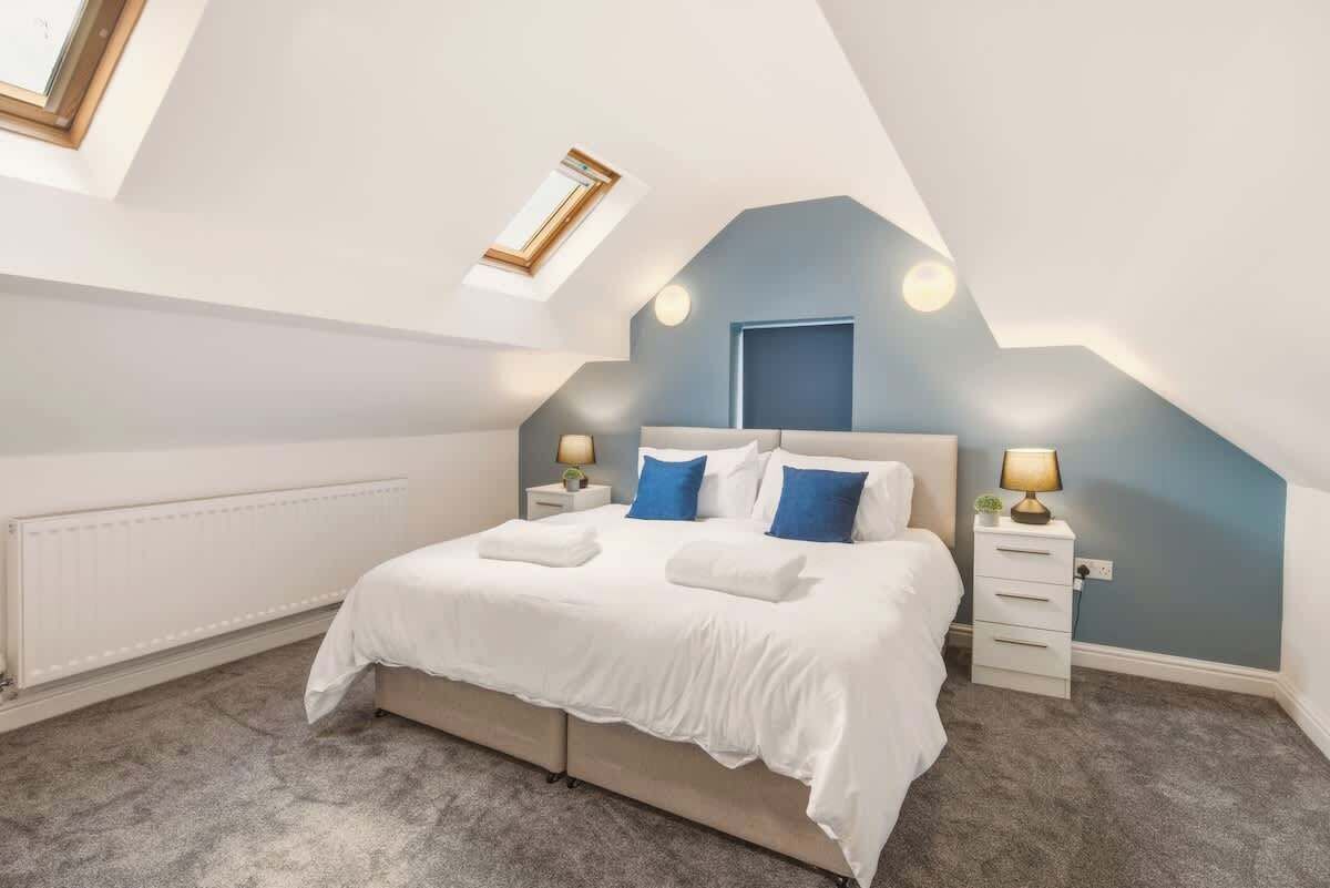 Een slaapkamer met schuine wand, een bed met witte beddengoed, twee nachtkastjes met lampen en een radiator.