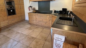 A kitchen with wooden cabinets, a built-in oven, a stove, a sink, and a countertop with a kettle and coffee maker.