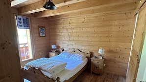 A wooden-paneled room with a bed, two bedside tables, a hanging light fixture, and a window with a view.