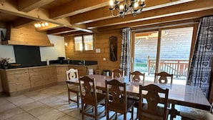 A wooden interior with a dining table, chairs, a chandelier, and a kitchen area.