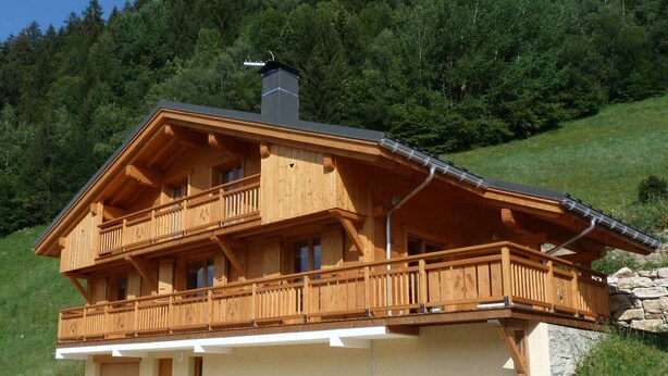 A wooden chalet with a balcony, a chimney, and a stone foundation.
