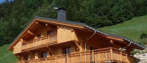 A wooden chalet with a balcony, a chimney, and a stone foundation.