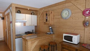 Pieni, käytännöllinen keittiö, jonka seinät ovat puuta, ja jossa on valkoinen jääkaappi, mikroaaltouuni, vedenkeitin ja kello.