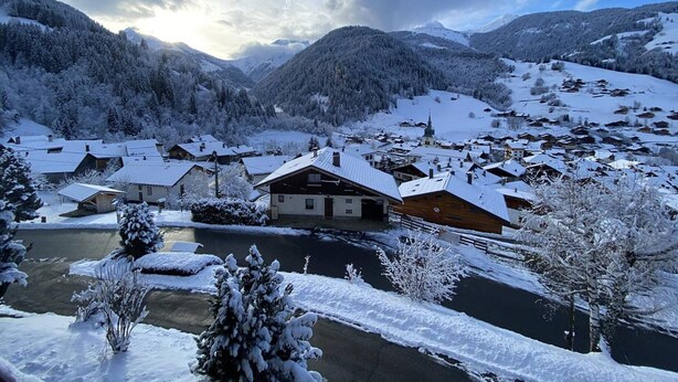Ein verschneites Dorf mit traditionellen Holzhäusern, einer Kirche und einem Fluss.