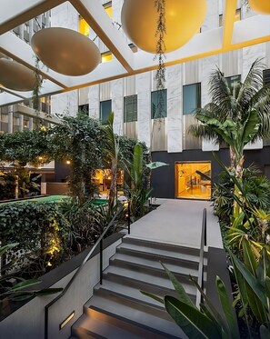 Un moderno atrio interior con una escalera central, rodeado de exuberante vegetación y un ambiente cálido y acogedor.