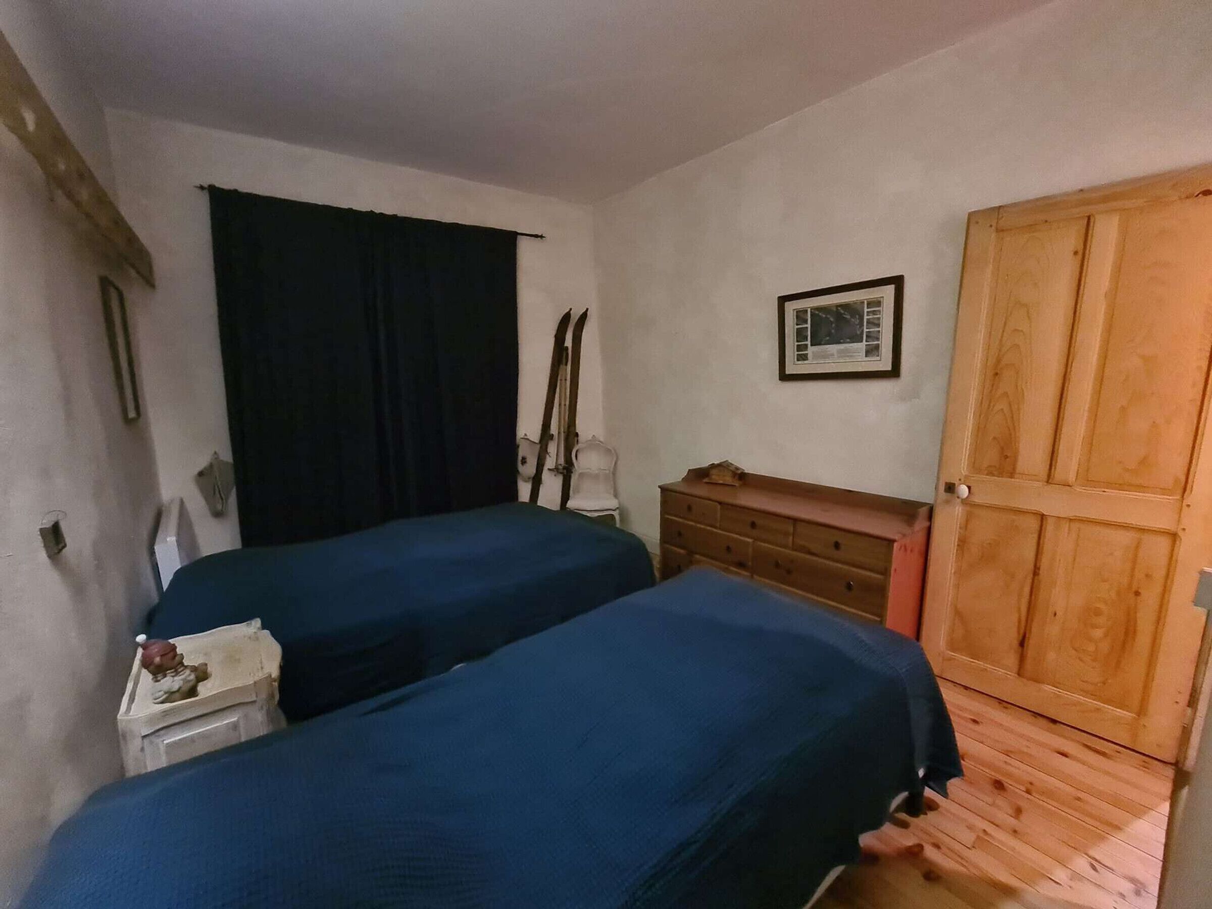 Een kamer met twee bedden, een houten garderobe, een ingelijst schilderij aan de muur en een raam met een zwart gordijn.